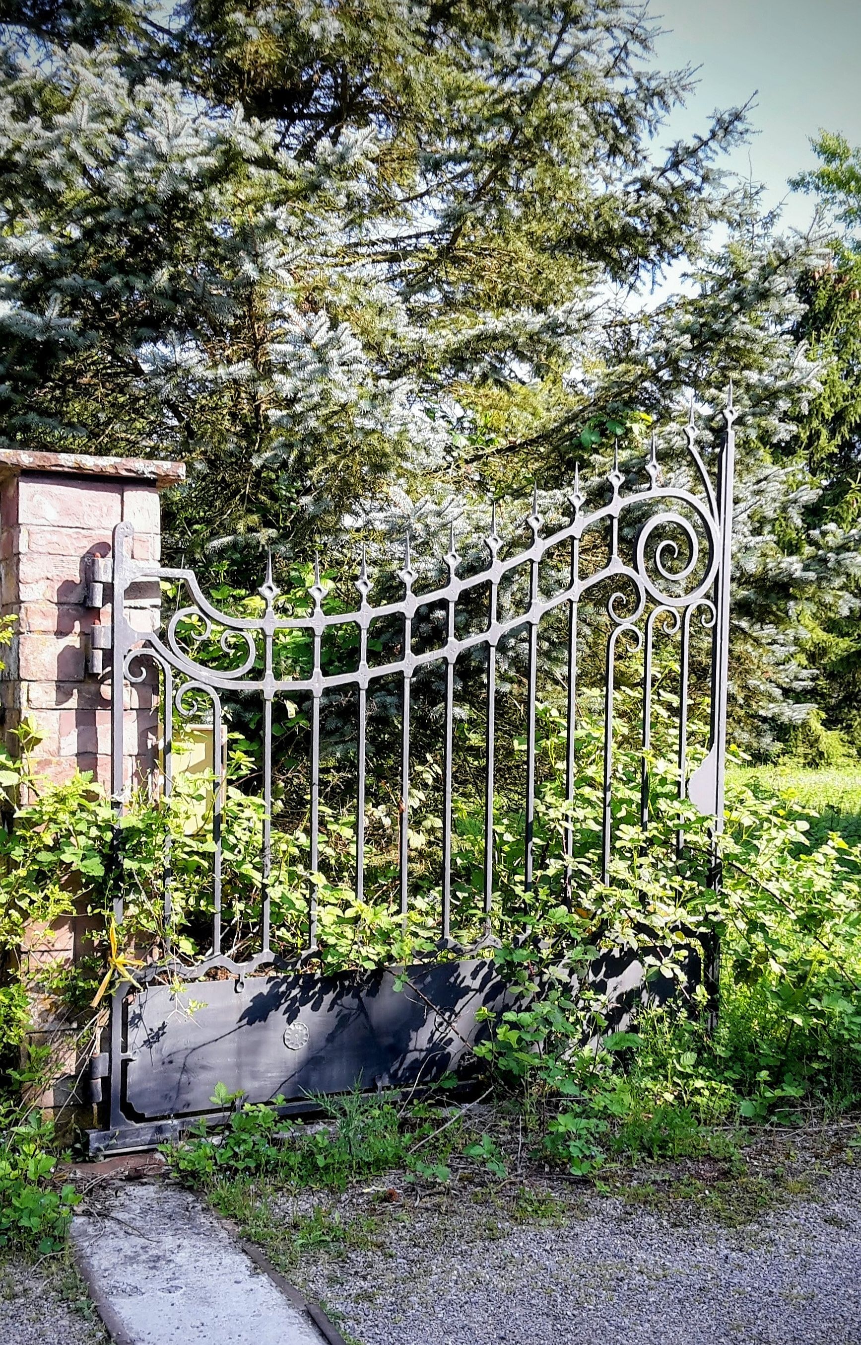 Sierlijke metalen tuinpoort naast een stenen pilaar.