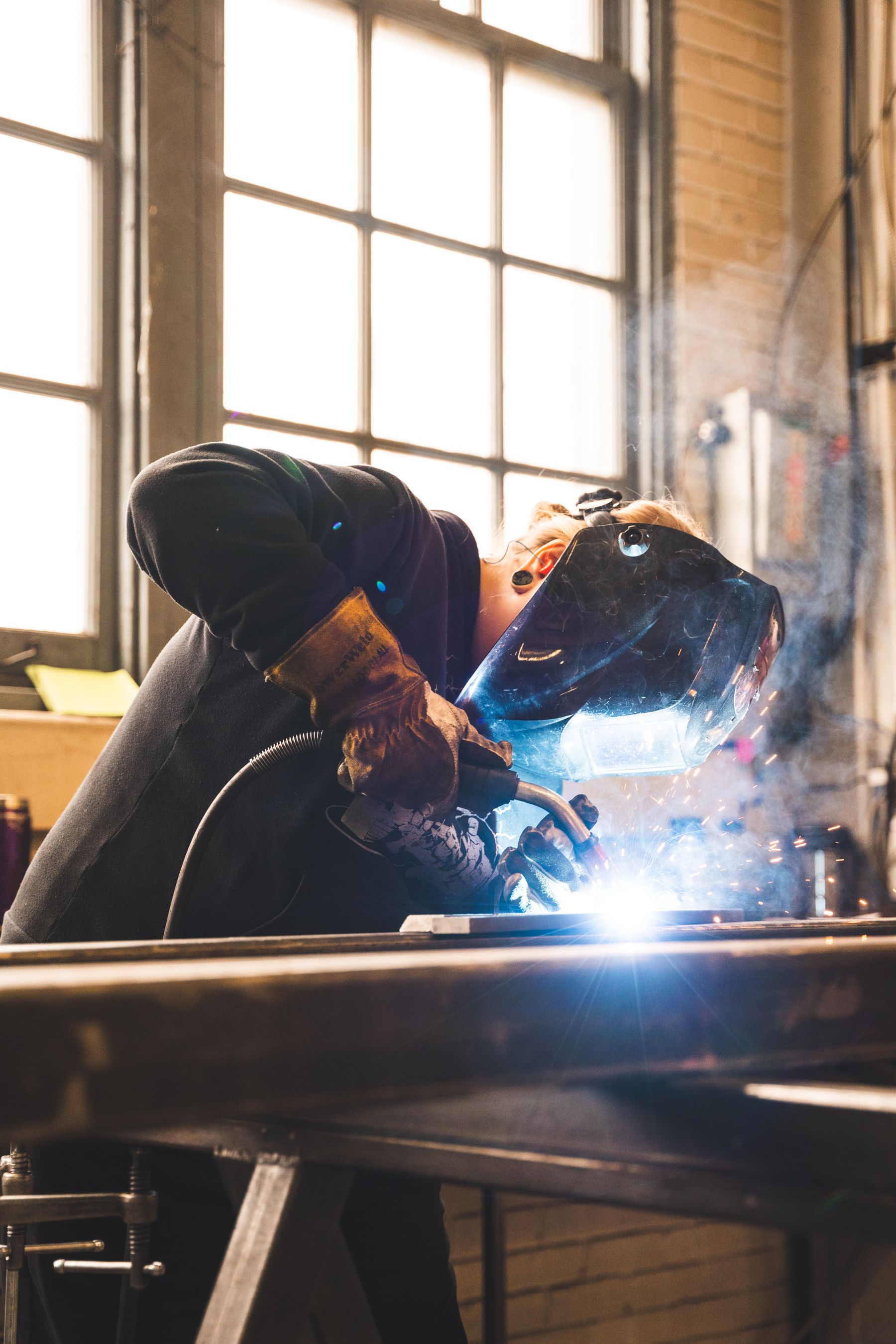 Lasser werkt aan een metalen onderdeel op een werkbank.